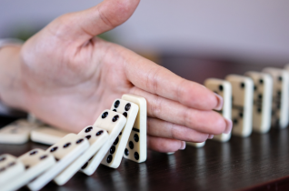 Woman's Hand Stopping a Chain of Dominos from Falling